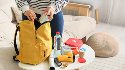 Young woman packing emergency backpack with necessities at home, closeup