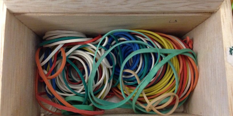 Small wooden box filled with rubber bands of various sizes and colors.