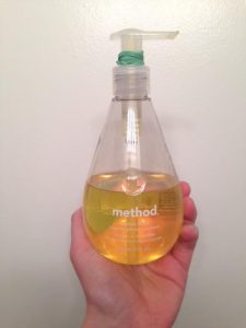 Hand holding up soap dispenser with rubber band tied around the nozzle.