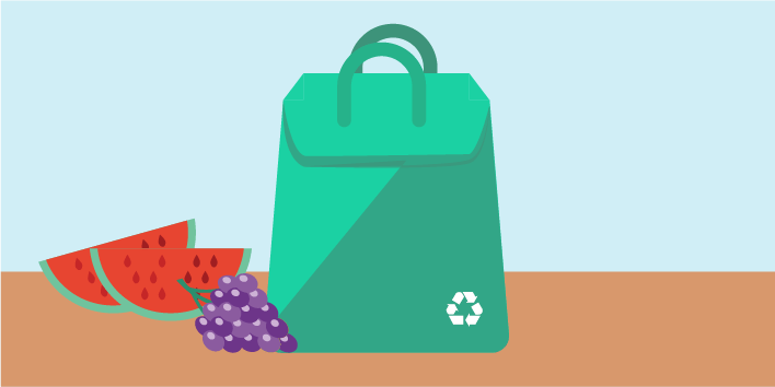 Reusable grocery bag with sliced watermelon and a bunch of grapes next to it.