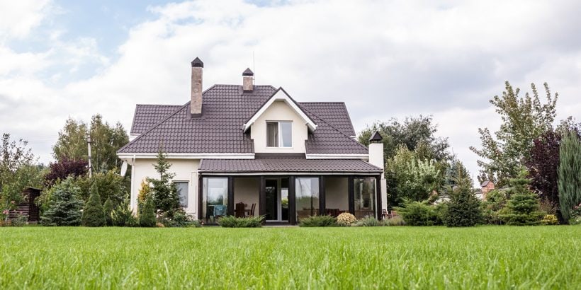 House with grey roof, surrounded by green grass and lush trees.
