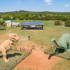 Green field with tyrannosaurus rex on the left, brontosaurus on the left and solar pavilion in the back.